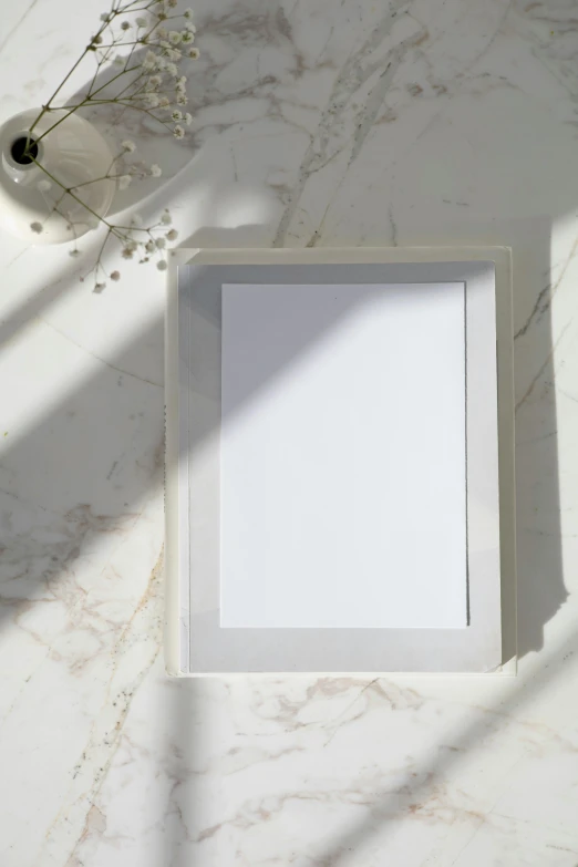 a picture frame sitting on top of a marble counter, a picture, gradient white to silver, on vellum, light grey backdrop, solid gray