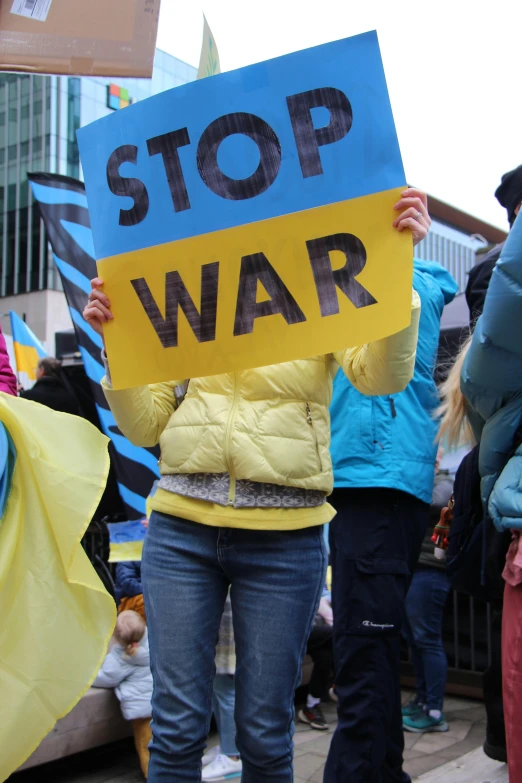 a woman holding a sign that says stop war, flickr, blue and yellow ribbons, war in ukraine, square, slide show