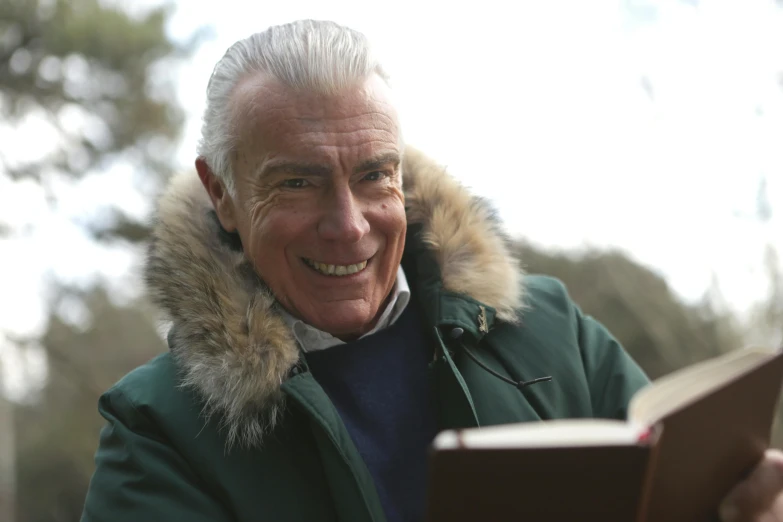 a man in a parka reading a book, inspired by Werner Andermatt, pexels contest winner, smiling at camera, geralt, 15081959 21121991 01012000 4k, ted danson