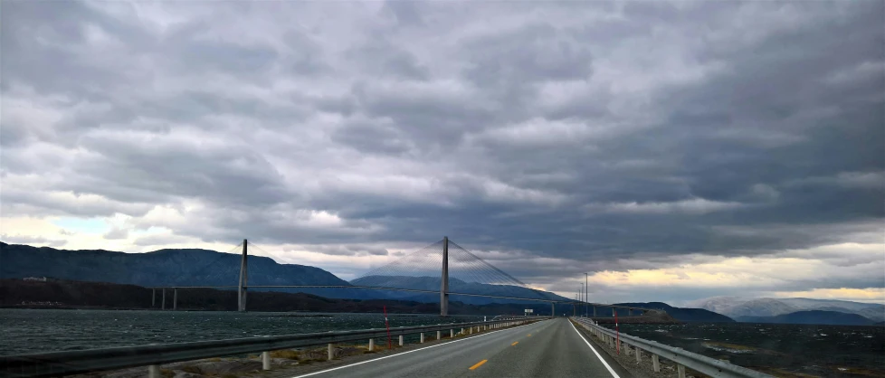 a highway next to a body of water under a cloudy sky, fjord, high bridges, instagram picture, youtube thumbnail