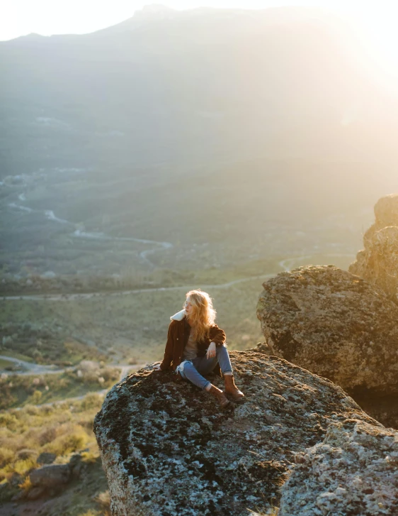 a woman sitting on top of a large rock, by Jessie Algie, unsplash contest winner, sun lit, samara weaving, smiling down from above, panoramic view of girl