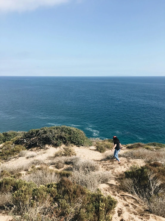 a person standing on top of a hill next to the ocean, hiking trail, profile image