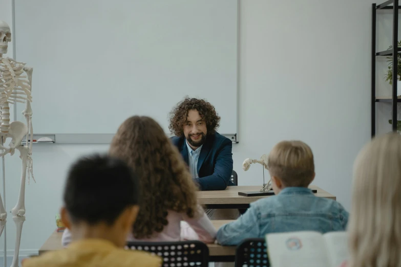 a man sitting at a table in front of a group of children, pexels contest winner, danube school, back to school comedy, ignant, lachlan bailey, giorgio a. tsoukalos