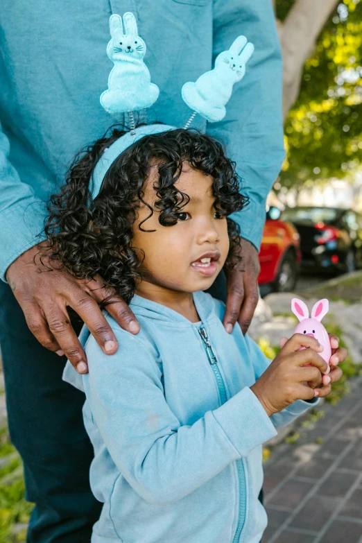 a man standing next to a little girl with bunny ears on her head, by Washington Allston, pexels contest winner, happening, curls, miffy, holding close, indian girl with brown skin