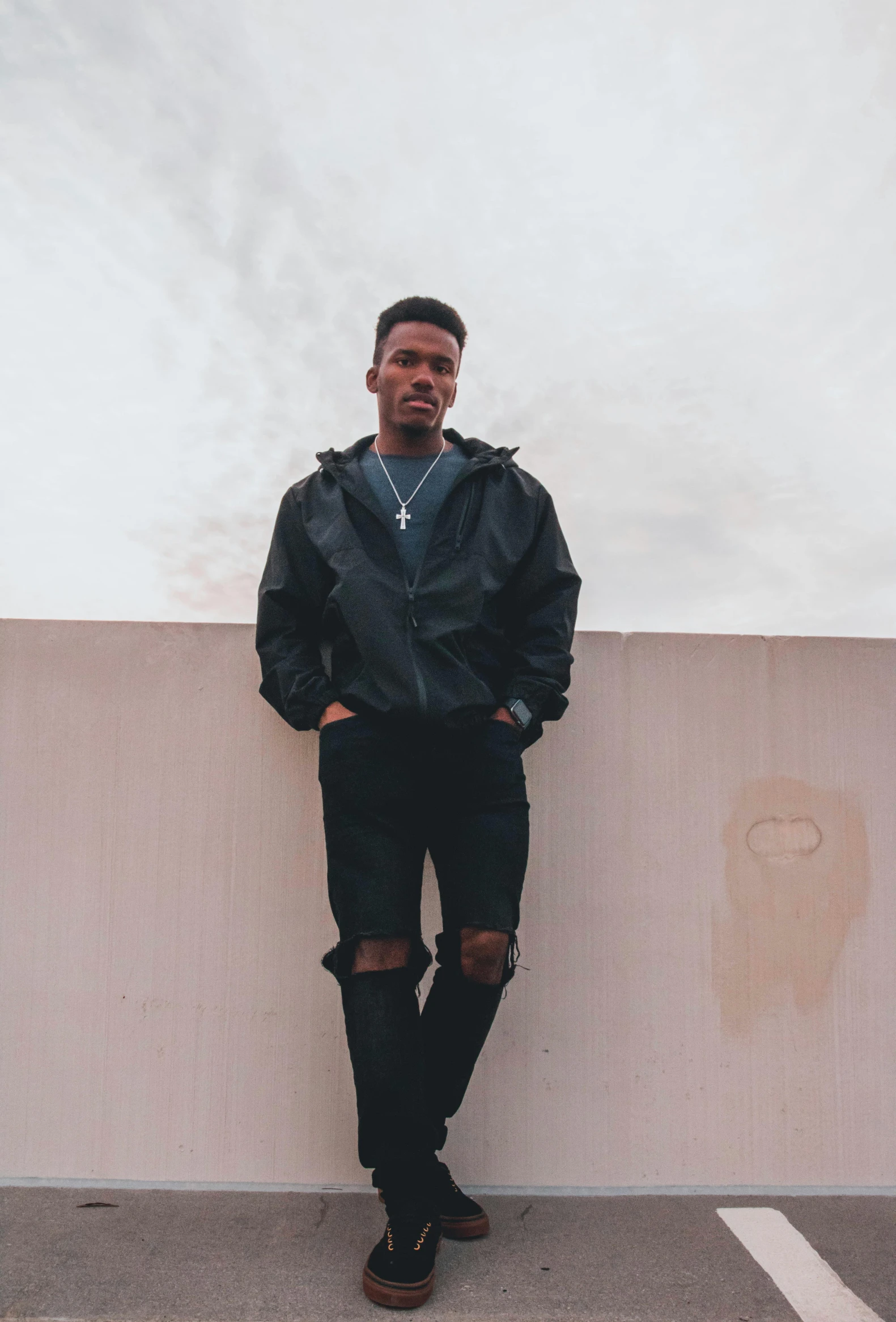 a man leaning against a wall in a parking lot, an album cover, trending on unsplash, black bomber jacket, non binary model, on a cloudy day, profile image