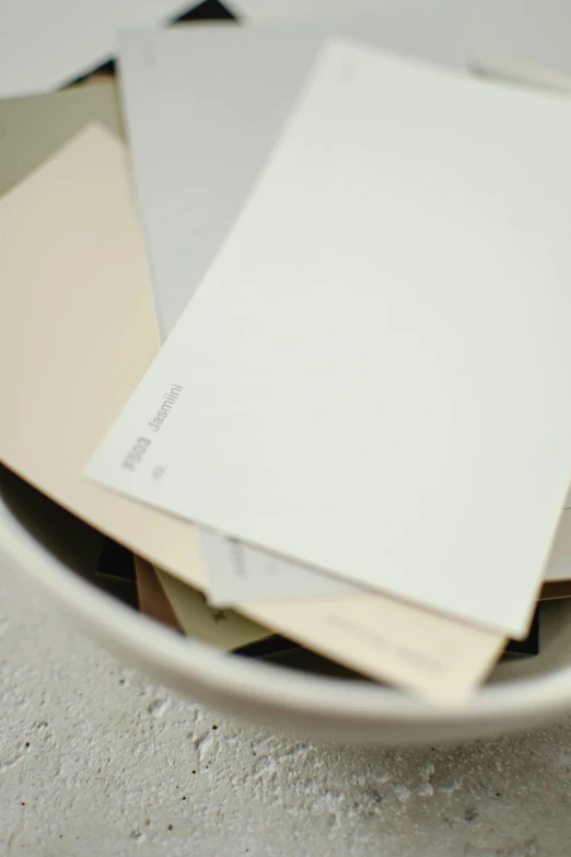 a bowl filled with papers sitting on top of a table, a picture, inspired by Rachel Whiteread, unsplash, postminimalism, matte paint colors, medium closeup, dieter rams, white plank siding