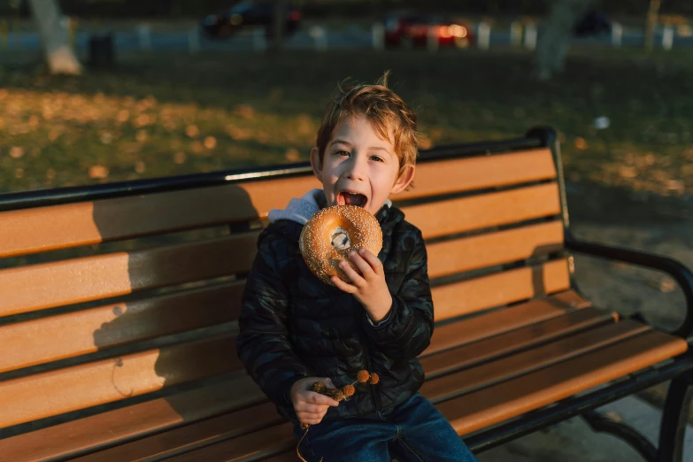 a young boy sitting on a park bench eating a donut, by Niko Henrichon, pexels contest winner, in the shape of a cinnamon roll, avatar image, ekaterina, cute boys