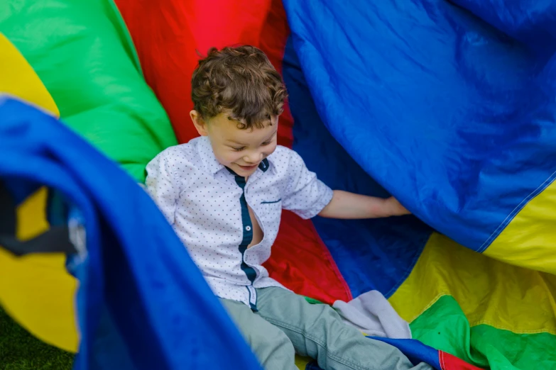 a young boy sitting on top of a parachute, by Samuel Scott, pexels contest winner, activity play centre, in a colorful tent, slides, high angle close up shot