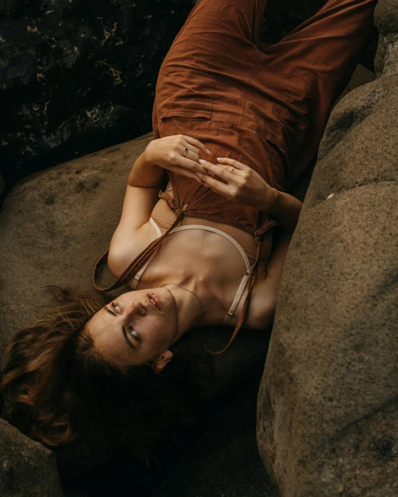 a woman laying on top of a large rock, inspired by Elsa Bleda, pexels contest winner, australian tonalism, top - down view, lovely woman, cavewoman, outside on the ground