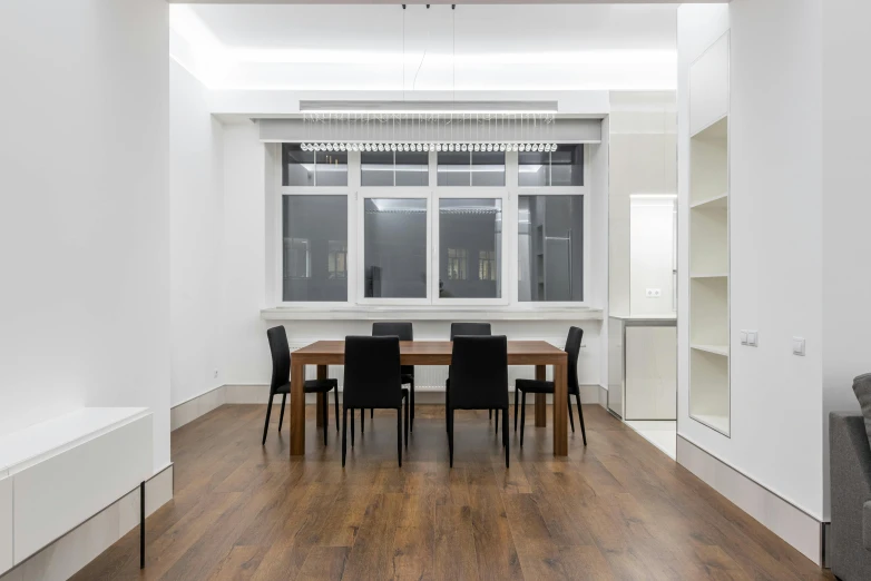 a dining room with a wooden table and black chairs, a 3D render, by Nina Hamnett, unsplash, light and space, cubical meeting room office, in a white room, oiled hardwood floors, wall to wall bookcases