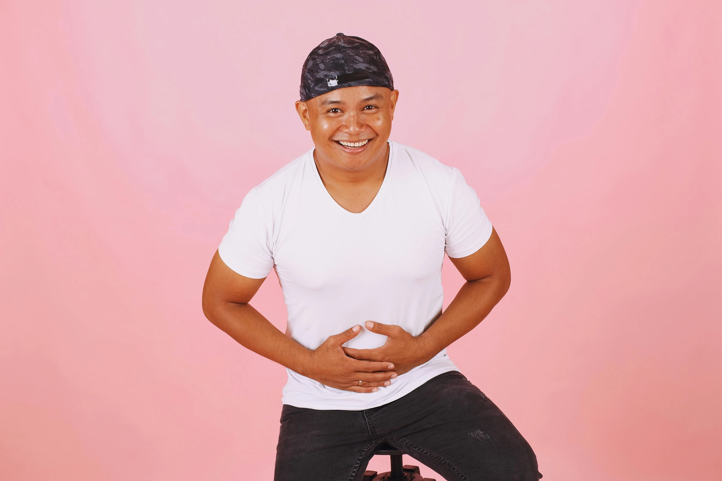 a man sitting on a stool in front of a pink background, inspired by Randy Vargas, happening, smileing nright, profile image, low quality photo, hero pose