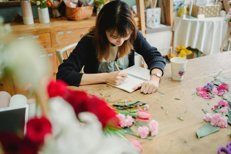 a woman sitting at a table working on flowers, a still life, by Julia Pishtar, pexels contest winner, writing in journal, emma bridgewater and paperchase, nishimiya shouko, profile image