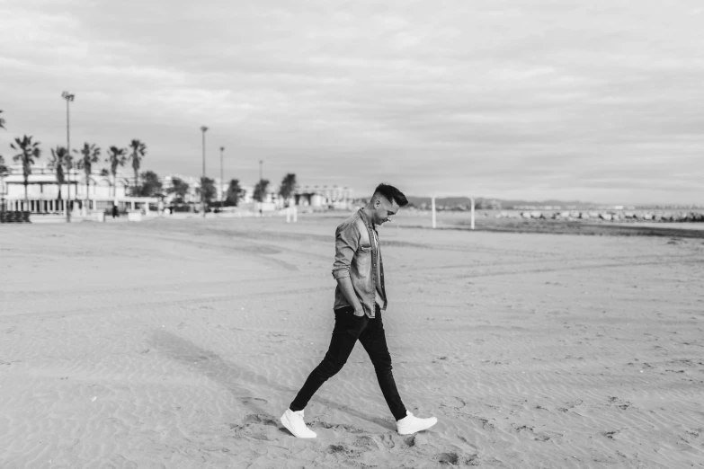 a black and white photo of a man walking on the beach, a black and white photo, by Daniel Gelon, pexels, realism, wearing a jeans jackets, skinny caucasian young man, new song, steve zheng