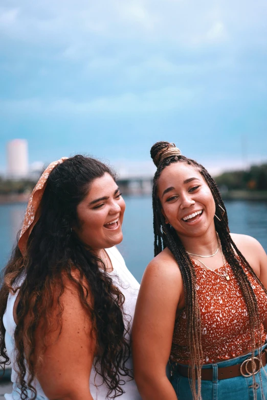 two women standing next to each other near a body of water, an album cover, by Washington Allston, trending on pexels, happening, wide grin, hispanic, headshot profile picture, in savannah