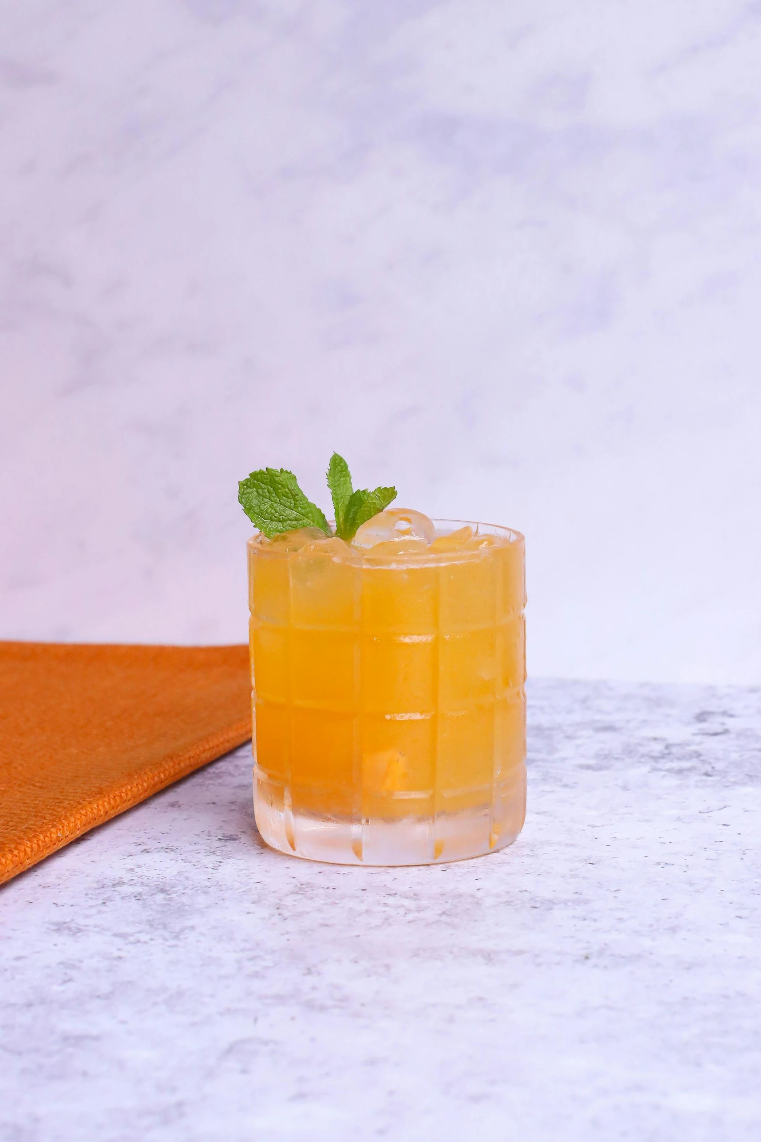 a glass of orange juice sitting on top of a table, drinks bourbon, mint, on a pale background, sassy pose