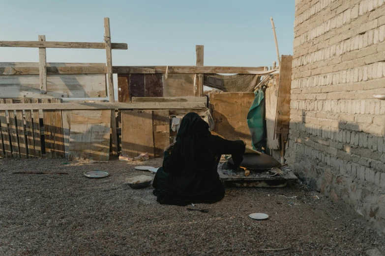 a woman sitting on the ground in front of a building, pexels contest winner, arte povera, portrait of bedouin d&d, makeshift house, view from the back, black