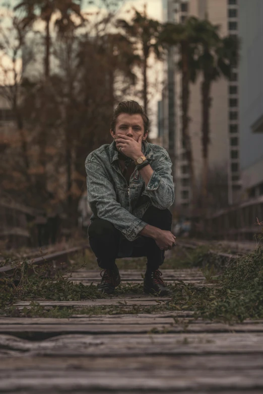 a man sitting on a train track in the middle of a city, by Ryan Pancoast, rick astley, promotional image, florida man, sorrow