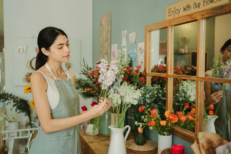 a woman arranging flowers in front of a mirror, pexels contest winner, arts and crafts movement, storefront, looking cute, bouquet, artist wearing overalls