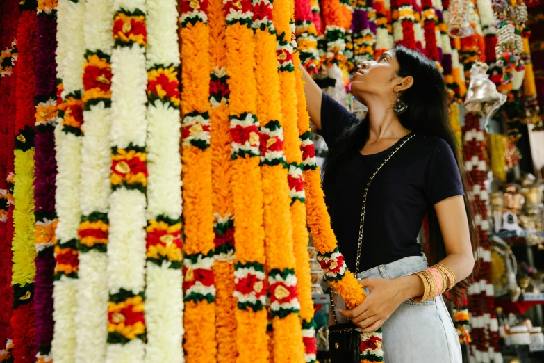 a woman standing in front of a wall of flowers, samikshavad, profile image, colorful adornments, excitement, displayed