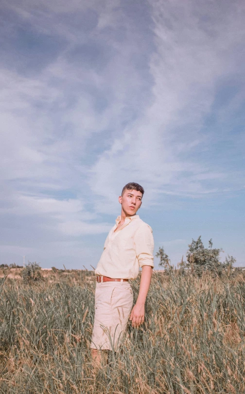 a man standing in a field of tall grass, an album cover, unsplash, lean man with light tan skin, full body photo, young greek man, profile image