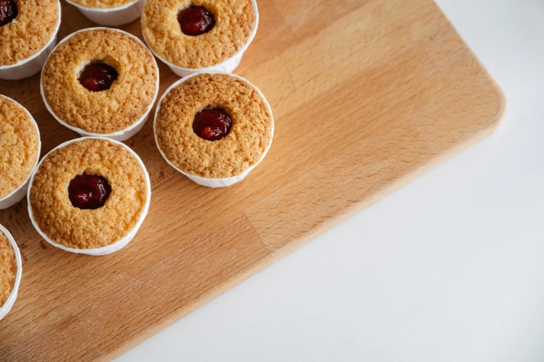 a wooden cutting board topped with mini cupcakes, by Andries Stock, pexels contest winner, mingei, red contact lenses, cookies, raspberry, slightly minimal