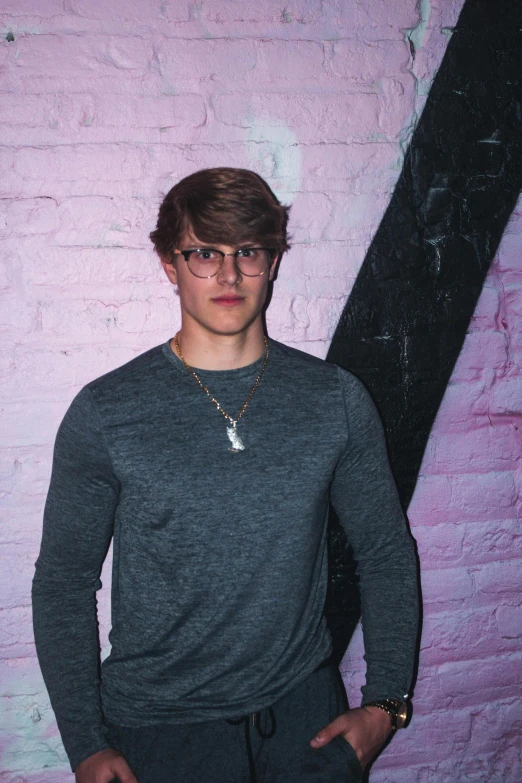 a young man standing in front of a brick wall, an album cover, inspired by John Luke, trending on pexels, big glasses, wax figure, blond boy, taken in night club