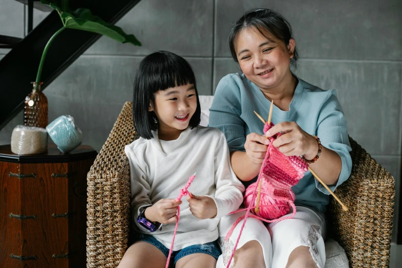 a woman sitting next to a little girl on a chair, inspired by Ruth Jên, pexels contest winner, yarn ball, avatar image, crafting, asian girl