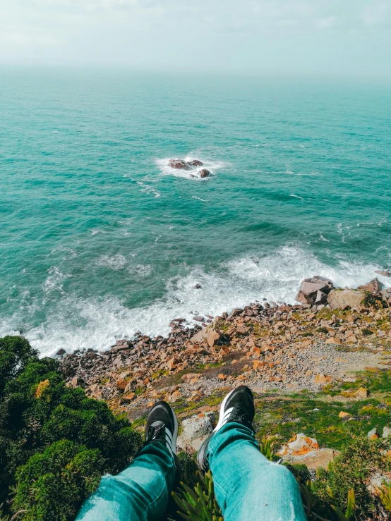 a person sitting on the edge of a cliff overlooking the ocean, flatlay, sneaker photo, wellington, pov photo