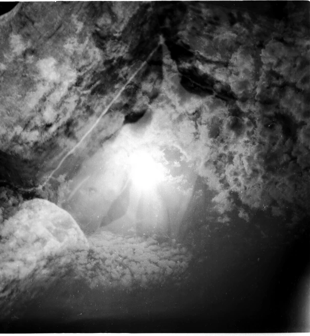 a black and white photo of a cave, inspired by Kim Keever, light and space, crepuscular ray, submarine camera imagery, underwater looking up, on the surface of an asteroid