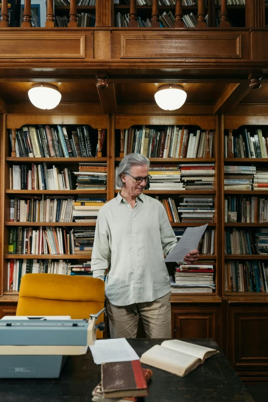 a man standing in front of a bookshelf in a library, an album cover, by Jakob Emanuel Handmann, gray haired, studying in a brightly lit room, julia hetta, medium-shot