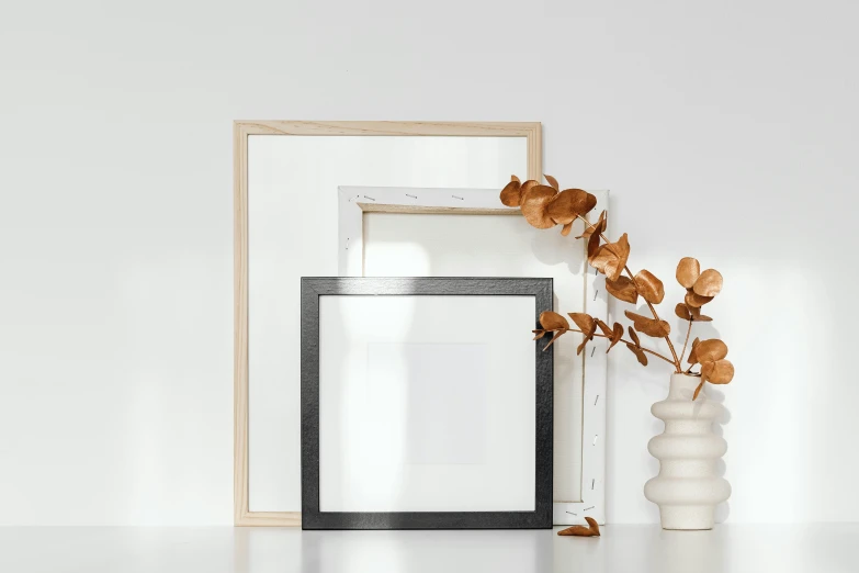 a picture frame sitting on top of a table next to a vase, a minimalist painting, pexels contest winner, branches and foliage, square pictureframes, various posed, architectural