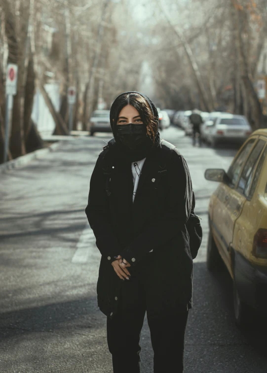 a woman standing in the middle of a street, an album cover, inspired by Elsa Bleda, pexels contest winner, realism, balaclava mask, tehran, wearing a black jacket, black car