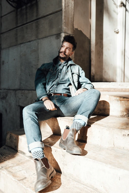 a man sitting on the steps of a building, wearing double denim, paolo veronese style, promotional image, wearing boots