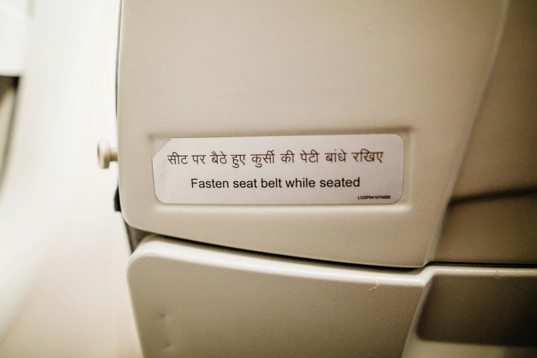 a close up of a toilet seat with a sign on it, by Bapu, airplane, language, white, flat