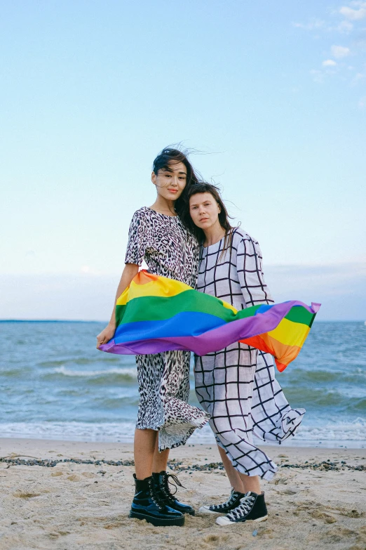 a couple of women standing on top of a sandy beach, pride month, issey miyake, bella poarch, square