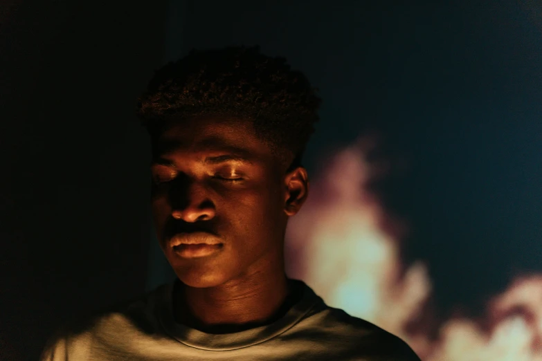 a close up of a person in a dark room, an album cover, pexels contest winner, black teenage boy, fire reflection, portrait soft light, solid background