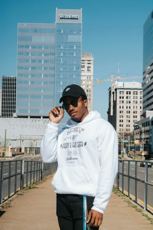 a man standing on a sidewalk talking on a cell phone, an album cover, inspired by Barthélemy Menn, unsplash contest winner, realism, hoodie, triple white colorway, corporate memphis, skyline