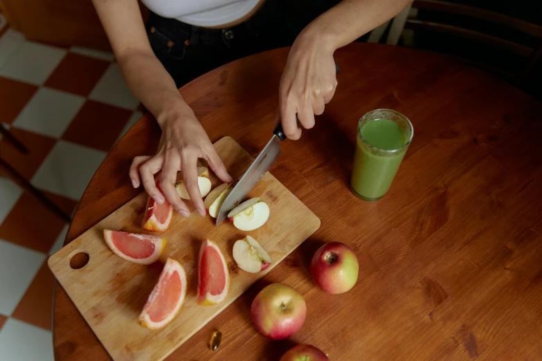 a person cutting a grapefruit on a cutting board, by Niko Henrichon, moringa juice, one holds apple in hand, holding magical kitchen knives, lena oxton