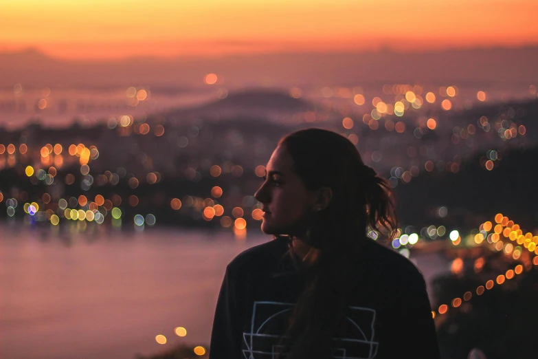 a woman looking out over a city at sunset, by Niko Henrichon, pexels contest winner, pretty lights, handsome girl, at night with lights, paradise in the background