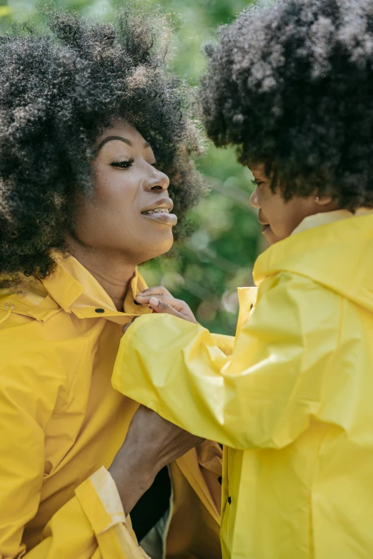 a couple of women standing next to each other, by Winona Nelson, trending on unsplash, visual art, yellow raincoat, with a kid, with afro, woman holding another woman