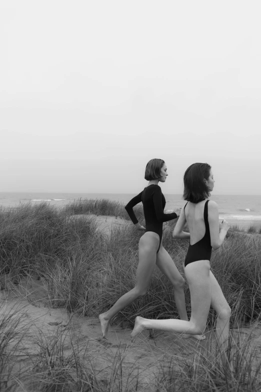 a couple of women standing on top of a sandy beach, a black and white photo, unsplash, conceptual art, wearing leotard, girl walking between dunes, ffffound, style of joel meyerowitz