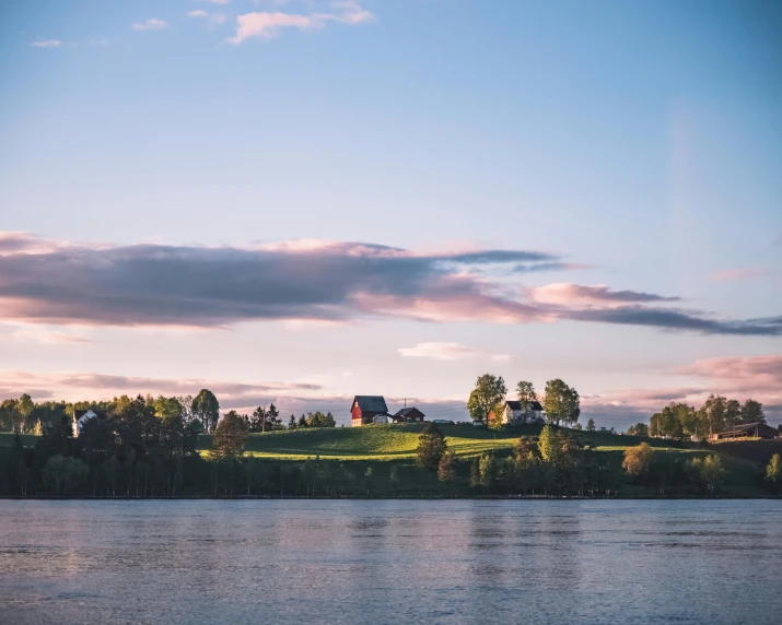 a large body of water next to a lush green hillside, by Jesper Knudsen, pexels contest winner, romanticism, helsinki, pink golden hour, next to a farm house and a barn, an island