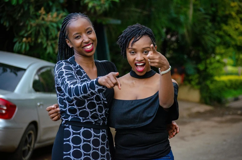 two women standing next to each other in front of a car, by Ingrida Kadaka, pexels contest winner, hurufiyya, large black smile, with pointing finger, very kenyan, avatar image