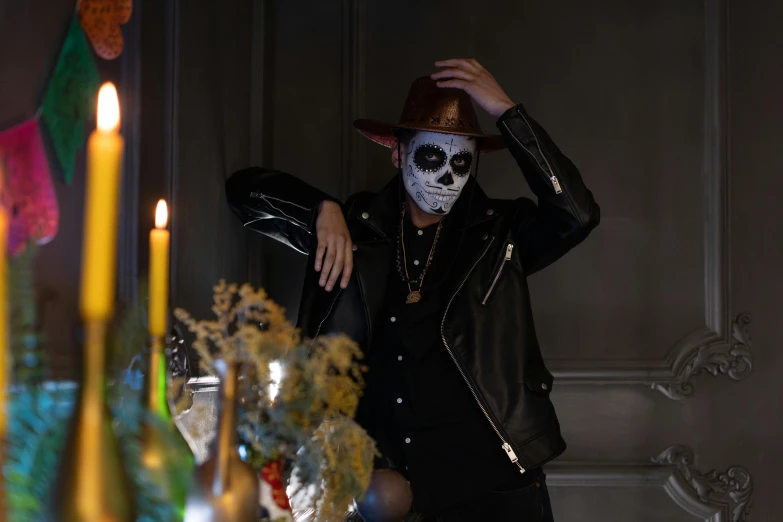 a man in a skeleton mask standing next to a table with candles, by Julia Pishtar, trending on pexels, wearing sombrero, wearing samcrow leather jacket, épaule devant pose, lachlan bailey