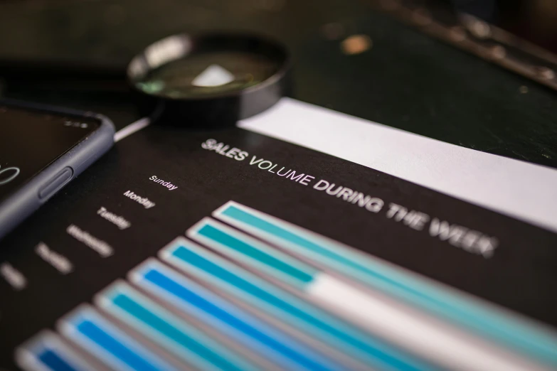 a cell phone sitting on top of a table next to a magnifying glass, a screenshot, by Daniel Lieske, unsplash, bar charts, black and teal paper, medium close up shot, volumetric