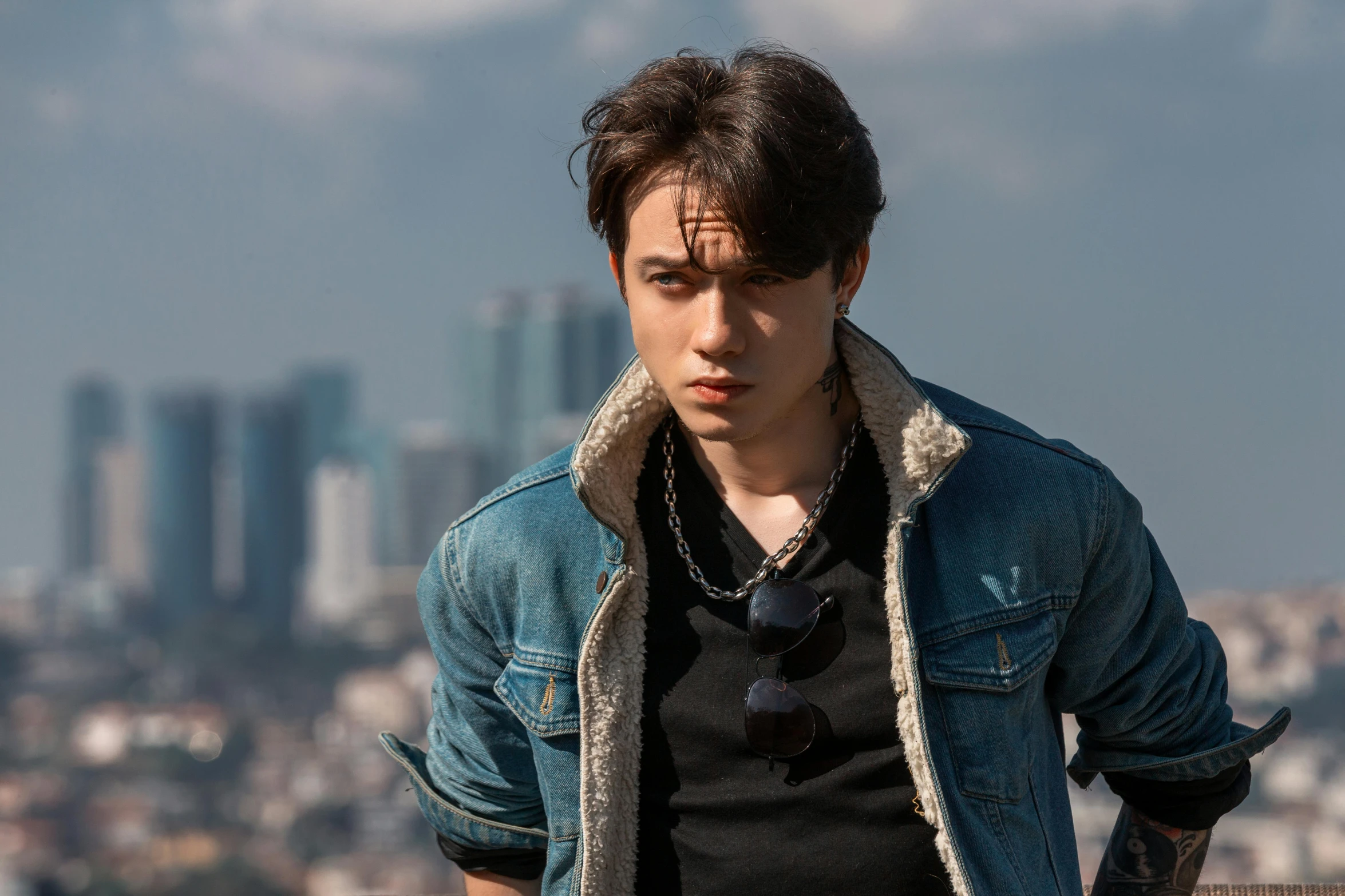 a man standing on a ledge with a city in the background, an album cover, inspired by Itō Ogura Yonesuke, pexels contest winner, photorealism, young man with beautiful face, wearing a jeans jackets, joe taslim, dilraba dilmurat