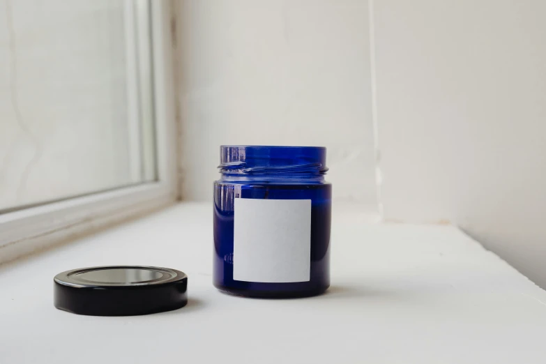 a blue glass jar sitting on top of a window sill, by Nina Hamnett, unsplash, candle wax, product label, on a white table, navy