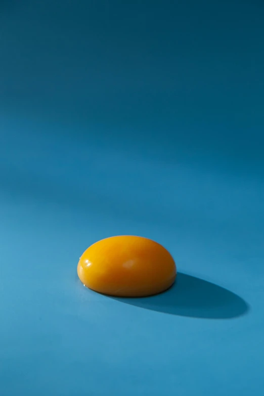 an egg sitting on top of a blue surface, by Doug Ohlson, caramel, cheddar, golden sun, super smooth