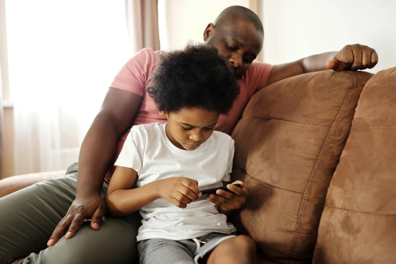 a man and a child sitting on a couch looking at a cell phone, pexels, black teenage boy, avatar image, the mome raths outgrabe, schools