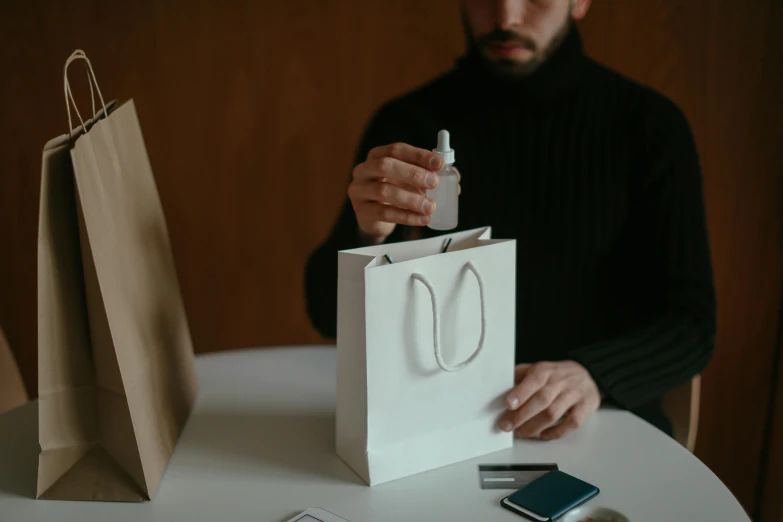 a man sitting at a table with a bag and cell phone, pexels contest winner, perfume, toy package, some pouring techniques, papercraft